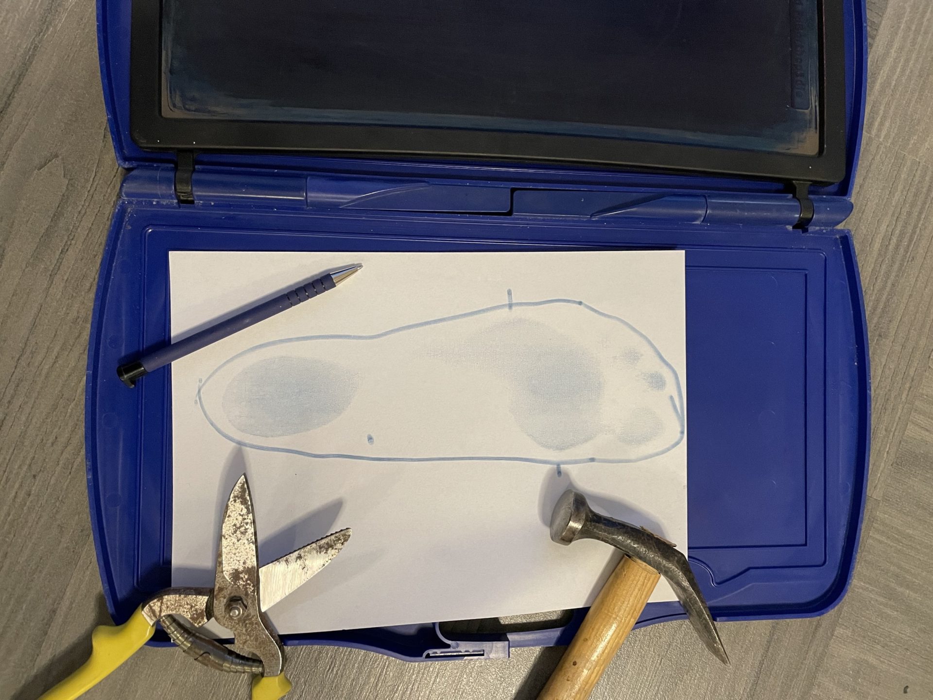 ein Blauabdruckkasten zum Maßnehmen für Einlagen daneben ein Hammer, eine Lederschere und Kugelschreiber